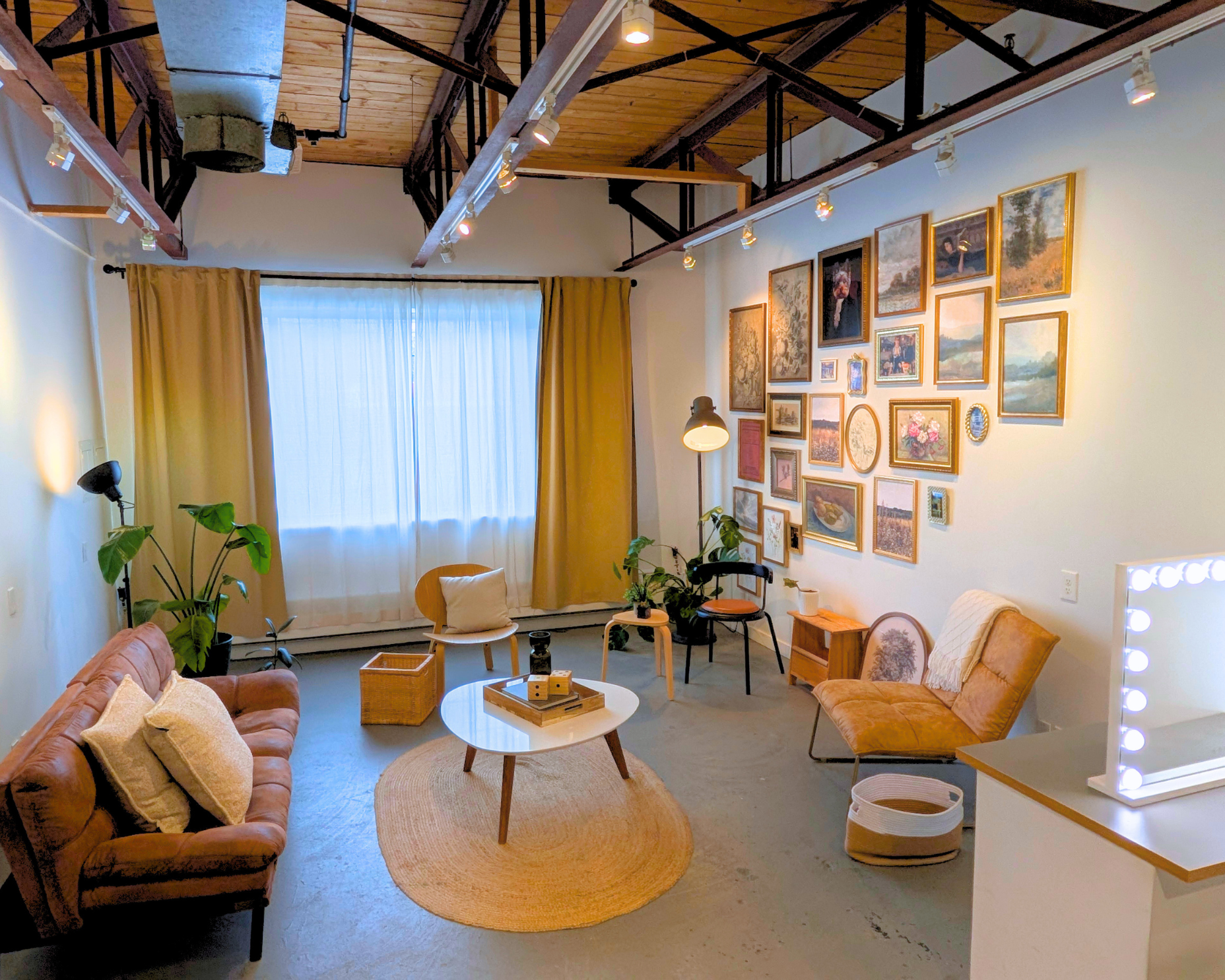 Studio living-room set with a two-seater sofa, accent chairs, coffee table, jute rug, plants, and gallery wall