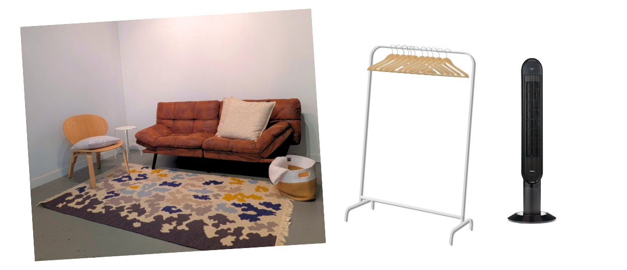 Waiting area with two-seater sofa, cushions, accent chair, rug, blanket basket, clothes rack, and tower fan